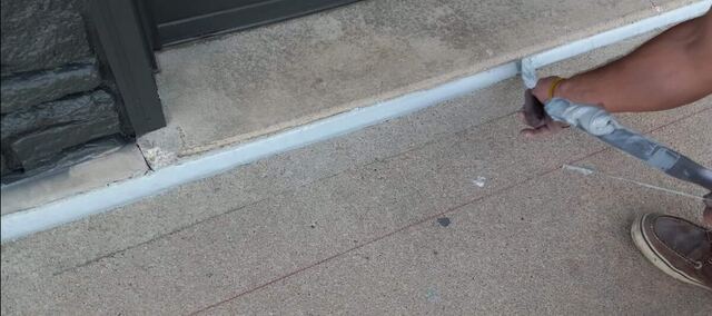 Crew member caulking a concrete step joint on an Omaha home